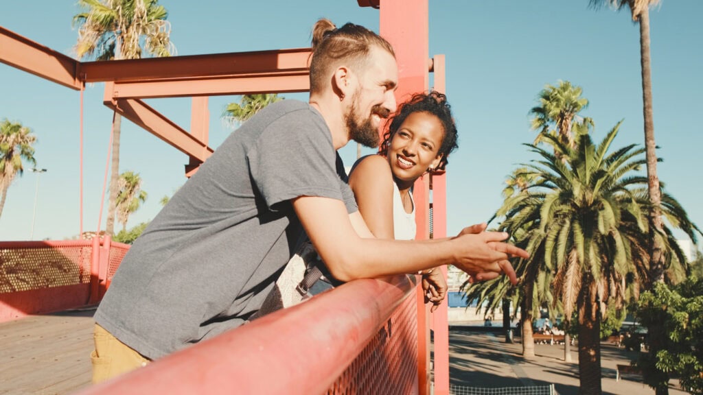Smiling couple sitting together on a bridge lined with palm trees.