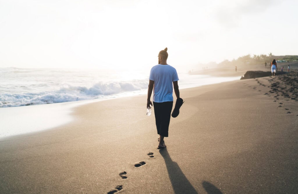 Man walking along a sandy beach at sunset.