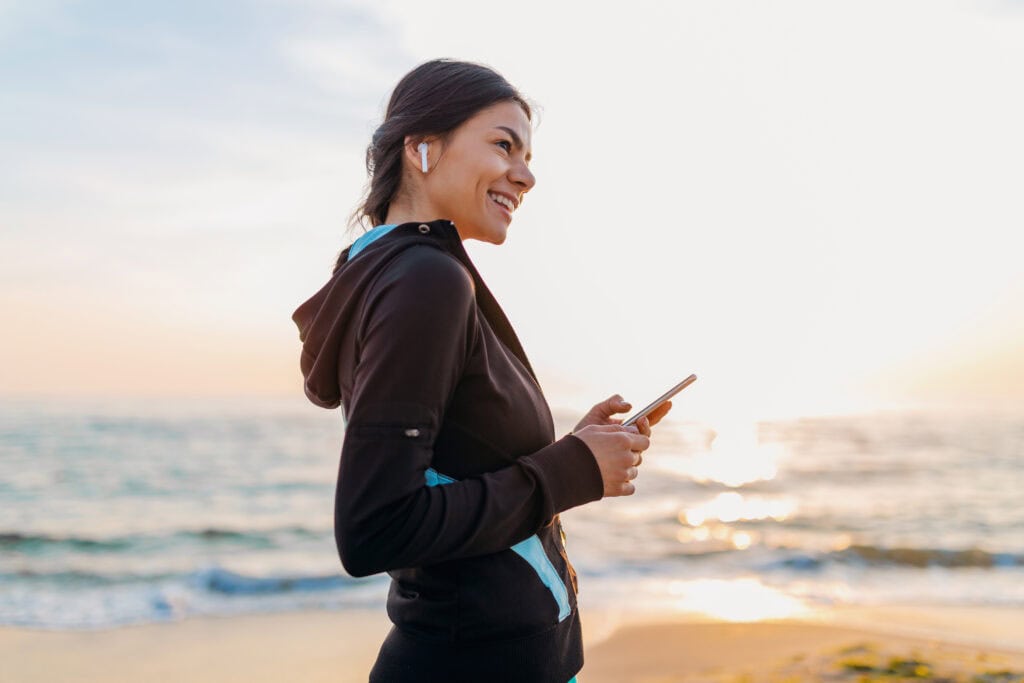 Woman smiling at her phone on the beach at sunset.